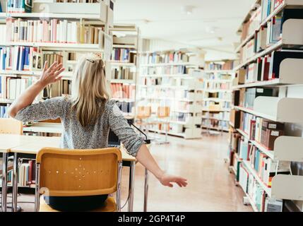 Müde Studentin sitzt am Schreibtisch mit einem Stapel Bücher, Universitätsbibliothek Stockfoto