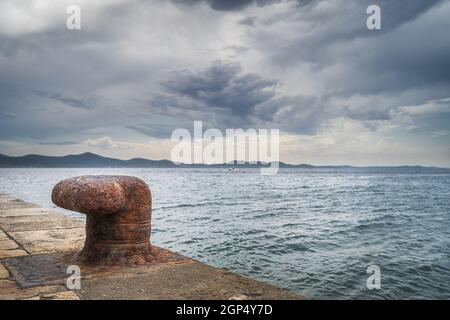 Single, alt und rostig Liegeplatz Poller auf dem Pier mit Blick auf die Adria und dramatischen Himmel in Zadar Bucht, Kroatien Stockfoto