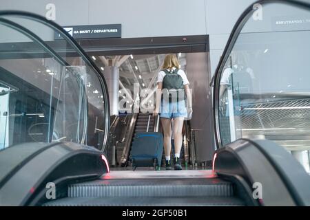 Blonde weibliche Touristin im Flughafenterminal, die an der Rolltreppe steht, um an einem internationalen Flughafen einzuchecken Stockfoto