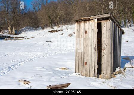 Eine alte hölzerne Straßentoilette steht allein auf einer leeren Schneebedecktes Grundstück Stockfoto