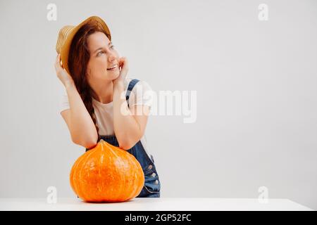 Frau in einem Hut steht auf weißem Hintergrund mit großen orangefarbenen Kürbis. Stockfoto