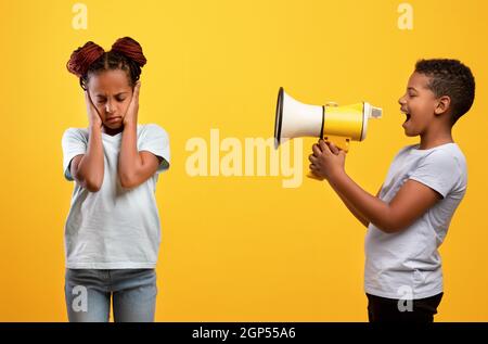 Frech afro-amerikanischen Jungen schrie seine ältere Schwester an, mit Megaphon, empörte schwarze Mädchen ihre Ohren zu schließen, während Geschwister schrie sie an, gelbe st Stockfoto