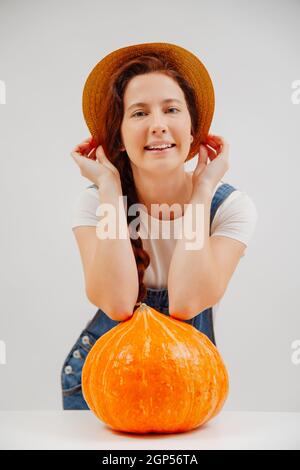 Lächelnde Frau im Jumpsuit auf weißem Hintergrund mit großem Kürbis. Stockfoto