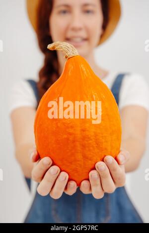 Kleiner orangefarbener Kürbis in den Händen eines verschwommenen Bauern ist senkrecht. Stockfoto