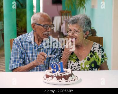 Ältere Paare mit einem Kuchen auf dem Tisch und die Nummer 91 auf dem Kuchen, und die Frau prüfend den Kuchen Stockfoto