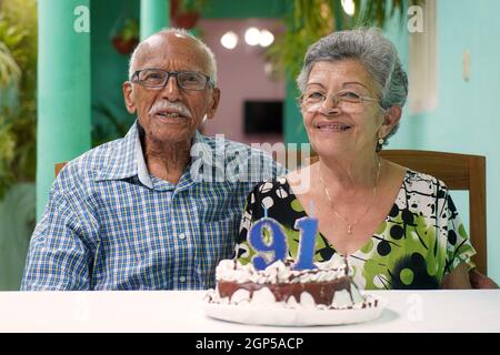 Ältere Paare mit einem Kuchen auf dem Tisch und die Nummer 91 auf dem Kuchen Stockfoto