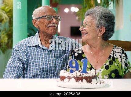 Ältere Paare mit einem Kuchen auf dem Tisch und die Nummer 91 auf dem Kuchen Stockfoto