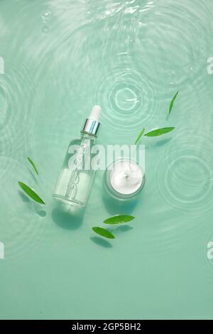 Set von feuchtigkeitsspendenden kosmetischen Produkten auf Wasser mit Tropfen. Glasflasche mit Pipette aus Serum, Kollagen, Glas Creme auf Aqua-Oberfläche mit Wellen-Konzept Stockfoto