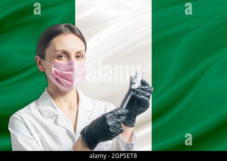 Ärztin bereitet die Impfung vor dem Hintergrund der Nigeria-Flagge vor. Impfkonzept Nigeria. Stockfoto