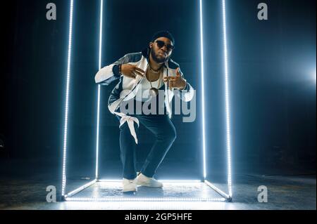 Stilvoller Rapper in Goldschmuck und Sonnenbrille, dunkler Hintergrund. Hip-Hop-Performer, Rap-Sänger, Break-Dance-Performer, Entertainment-Lifestyle Stockfoto