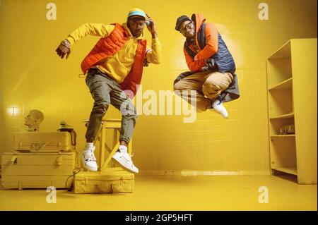 Zwei stylische Rapper mit Goldschmuck im coolen Studio, gelber Hintergrund. Hip-Hop-Darsteller, trendige Rap-Sänger, Breakdancer Stockfoto