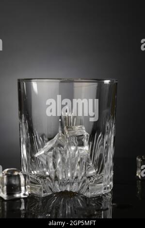 Auf der Theke wird ein Kristall-Whiskey-Glas mit etwas frischem Eis zubereitet. Stockfoto