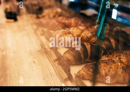 Der Kellner zieht Croissants in einem Cafe-Fenster heraus. Unscharfer Hintergrund. Hochwertige Fotos Stockfoto