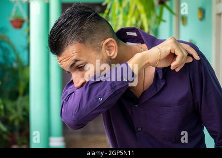 Ein junger Mann, der seinen Mund und seine Nase mit seinem gebogenen Ellbogen bedeckt Stockfoto