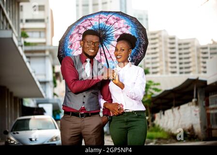 Porträt eines jungen afrikanischen Paares, das unter einem Regenschirm auf der Straße steht und lächelt Stockfoto