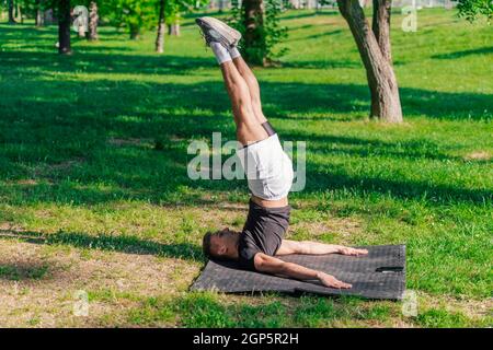 Junger sportlich schöner Mann, der Yoga im Park praktiziert und die Pflug-Pose macht. Stockfoto