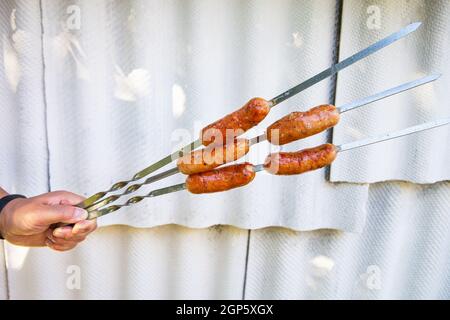 Bayerische Grillwürste, heiße Würste am Spieß. Grill in der Hand unter freiem Himmel auf weißem Hintergrund Stockfoto