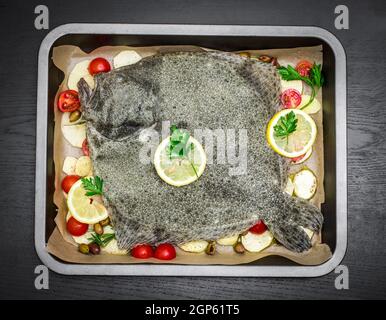 Tablett mit rohem Steinbutt-Fisch mit Kartoffelscheiben, gewürzt mit Olivenöl, Kirschtomaten, schwarzen Oliven, Petersilie- und Zitronenscheiben, fertig zum Kochen Stockfoto