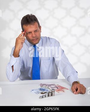Eine lateinische Mann vor einer Gruppe von Banknoten und Münzen mit einem denken oder die Berechnung der Ausdruck auf seinem Gesicht sitzen Stockfoto