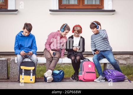 Kinder mit Rucksäcken sitzen auf der Bank im Park in der Nähe der Schule. Menschliche Beziehungen. Junge Generation. Stockfoto