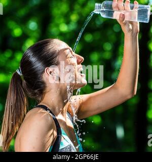 Nahaufnahme Gesichtsaufnahme des jungen Fitness-Mädchen gießen kaltes Wasser auf das Gesicht nach jogg.woman im Wald vor grünem Hintergrund. Stockfoto