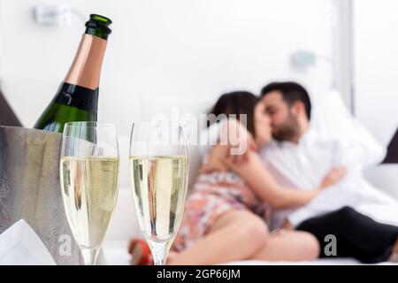 Nahaufnahme Champagner-Gläser und kalte Flasche im Eisküssen mit küssenden Paar im Hintergrund. Stockfoto