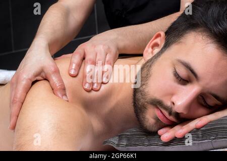 Nahaufnahme der Physiotherapeutin dong Heilung Schultermassage auf jungen Mann. Stockfoto