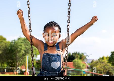 Nahaufnahme des glücklichen afrikanischen Kindes, das im Park auf Schaukel die Arme hebt. Stockfoto