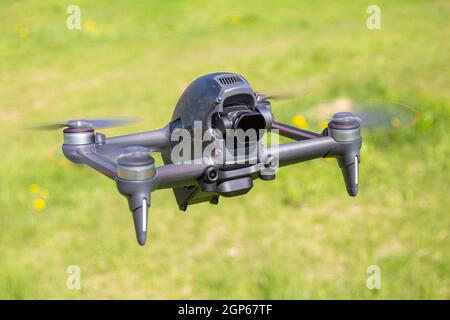 Die neue FPV-Drohne fliegt an einem sonnigen Tag auf Gras im Beckground. Vorderansicht Von Oben. Headless Quadcopter mit digitaler 4K-Kamera mit 60 Bildern/s und Remote-Controller Stockfoto