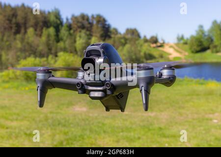 Die neue FPV-Drohne fliegt an einem sonnigen Tag auf Gras im Beckground. Vorderansicht Von Oben. Headless Quadcopter mit digitaler 4K-Kamera mit 60 Bildern/s und Remote-Controller Stockfoto