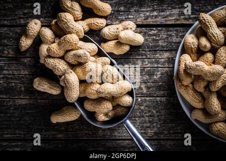 Geröstete Erdnüsse. Leckere Erdnüsse in Metalllöffel auf Holztisch. Draufsicht. Stockfoto