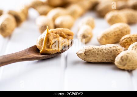 Erdnussbutter in Holzlöffel und Erdnüsse auf weißem Tisch. Stockfoto
