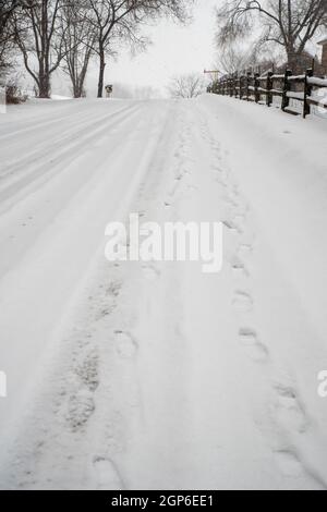 In diesem vertikalen Bild erstrecken sich zwei lange Fußabdrücke auf einem verschneiten Hügel. Schneeflocken fallen für die Reise. Tageslicht mit Kopierbereich. Stockfoto