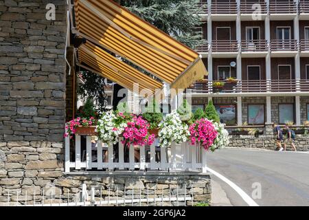 Courmayeur, Italien - August 24 2021: Gelbe, gestreifte, aufziehende Markise über dem Restaurant mit Platz im Freien zum Essen mit Blumen um den Zaun Stockfoto