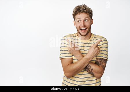 Fröhlicher blonder Mann zeigt die Finger seitwärts, zeigt linke und rechte Geste, lächelt und lacht glücklich, zeigt die Auswahl der Ladenprodukte, steht Stockfoto
