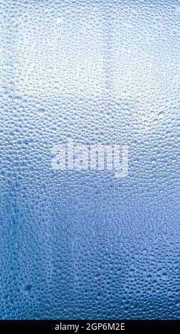 Regentropfen auf dem Glas bei Regenwetter.die glitzernde, glänzende Wasseroberfläche auf dem Glas.Wassertropfen in Form von Kugeln oder Kugeln.Blaue Regentropfen bac Stockfoto