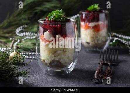 Traditioneller russischer Festsalat Hering unter einem Pelzmantel in portionierten Gläsern auf dunkelgrauem Hintergrund Stockfoto