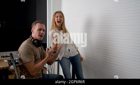 Toningenieur und Sänger zeigen nach Abschluss der Arbeit Zeichen der Freude. Musiker, die Musik im professionellen Aufnahmestudio produzieren. Stockfoto