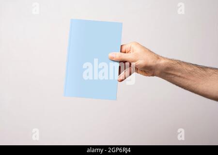Männliche Hand mit geschlossenem Buch-Katalog mit leerem Cover, Modell-Serienvorlage bereit für Ihr Design, Buchcover-Auswahlweg ausgeschlossen. Stockfoto