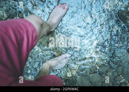 Ausschneiden der männlichen barfuß Füße mit roter Hose wandern in einer seichten Fluss Stockfoto