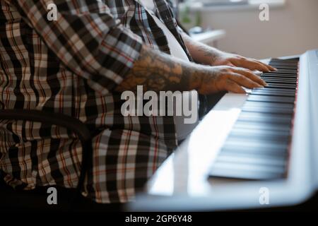Komponist mit Übergewicht spielt Musik auf einem modernen Synthesizer, der im hellen Raum sitzt Stockfoto