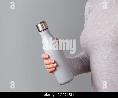 Nahaufnahme der Frau in grau T-Shirt mit grau isoliert Flasche auf grauem Hintergrund Stockfoto