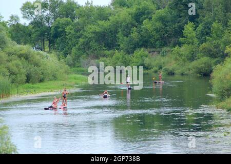 Eine Gruppe von Menschen segelt auf Kajaks entlang eines wunderschönen Flusses. Sommerferien. Sport und Erholung auf dem Fluss im Sommer. Kajakfahren auf dem Fluss. F Stockfoto