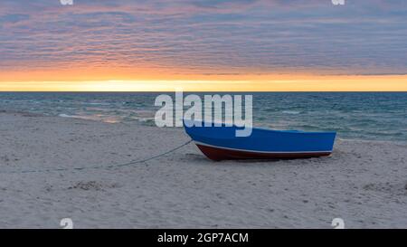 Blaues Boot am Strand an der Ostsee bei Sonnenuntergang Stockfoto