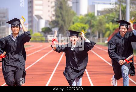 Glückliche Abschlussstudenten mit Diplom und laufen auf dem Stadion In der Schule Stockfoto