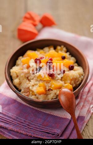 Hirse-Porrige mit Kürbis in Tonschale mit Holzlöffel auf Holzboden Stockfoto