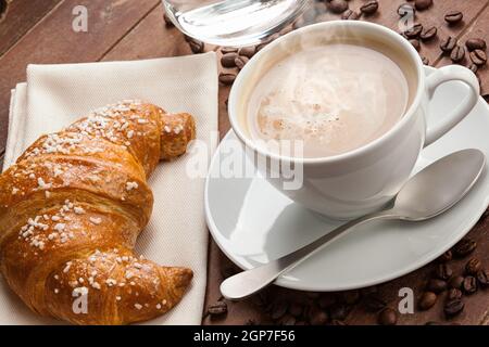 Cappuccino mit Croissant und ein Glas Wasser in die Schale mit dunkelbraunem Holz. Stockfoto