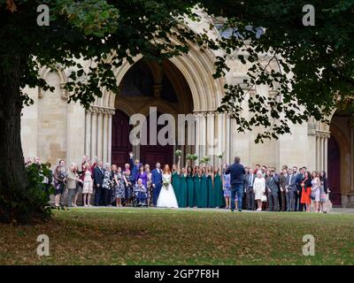 St Albans, Hertfordshire, England, September 21 2021: Herbstliche Hochzeit vor der Kathedrale, während die Brautjungfern Blumensträuße für ein Pho in der Luft halten Stockfoto