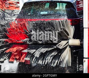 Schwarzes Auto in automatische Autowäsche rotierende rote und schwarze Bürste. Waschen des Fahrzeugs. Stockfoto