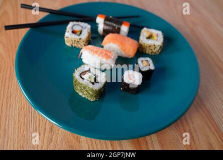 Sushi auf einem grünen Teller mit Essstäbchen arrangiert Stockfoto